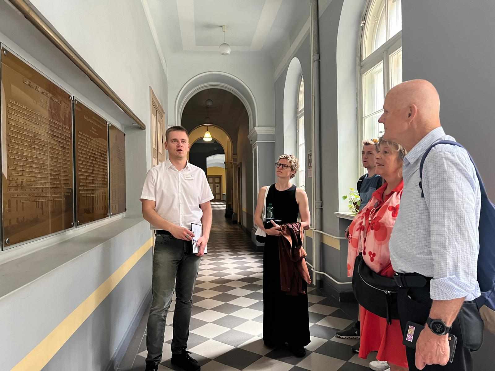 LU Muzeja krājuma glabātājs Rūdolfs Rubenis iepazīstina Hilda ģimeni ar LU mecenāta sienu (foto: Sarmīte Livdāne)